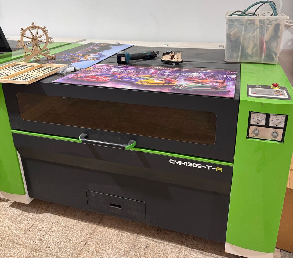 מכונת לייזר CO2 גדולה בצבע ירוק, ועליה לוח שש בש ודגם עץ של גלגל ענק.