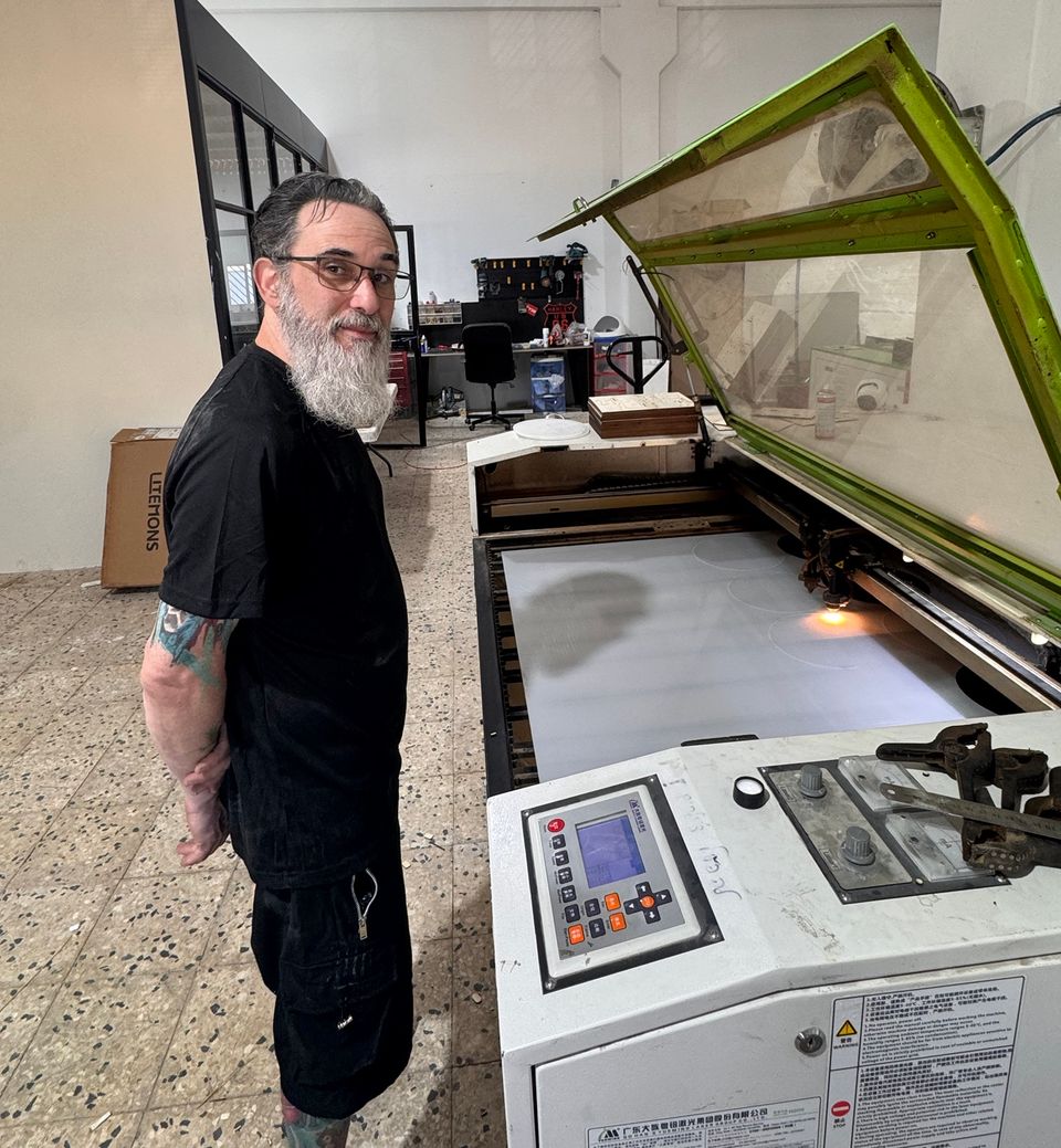 גילי מחייך ליד מכונת לייזר גדולה בזמן חיתוך של פרספקס לבן.